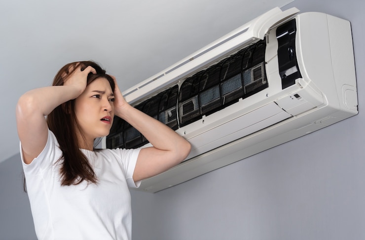 Woman frustrated with aircond problems in Malaysia while checking a malfunctioning indoor unit